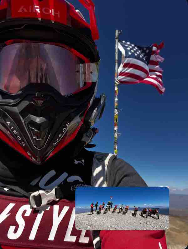 Dual-sport rider at a summit beside a flag